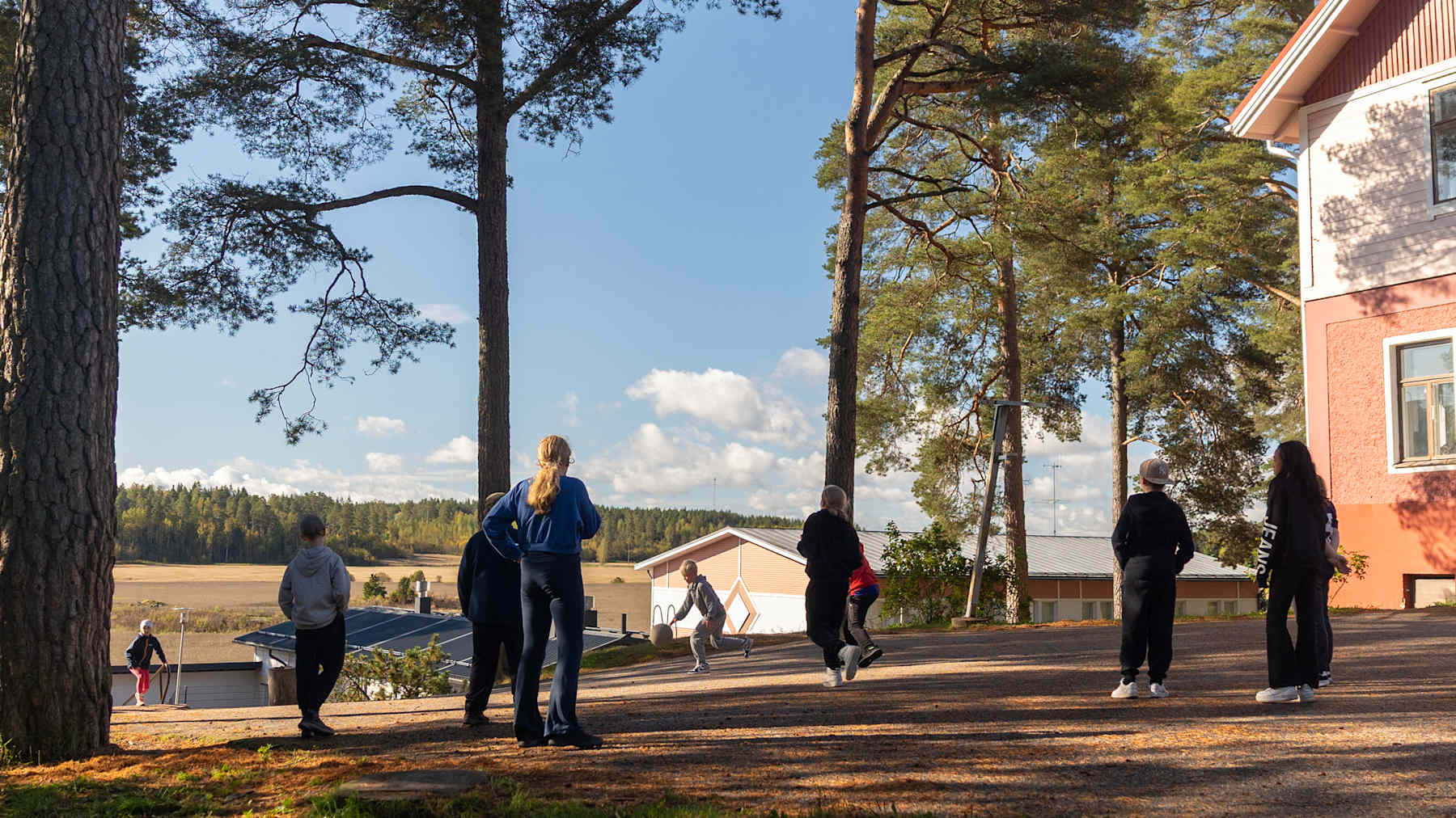 Oppilaita pelaamassa koulun pihalla, taustalla näkyy peltomaisema.