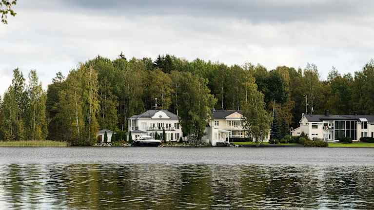 Kolme valkeaa taloa järven rannassa.