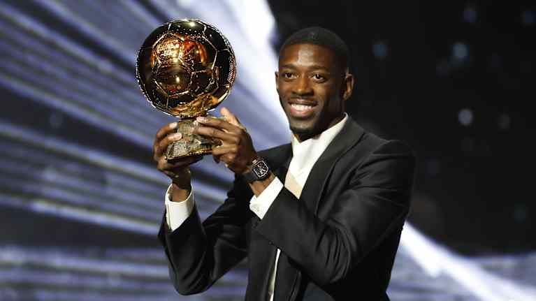 Jalkapalloilija Ousmane Dembele poseeraa Kultainen pallo -palkinnon kanssa puku päällään.