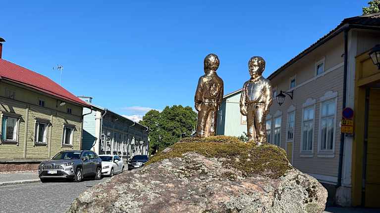 Veistoksessa on kaksi kultaista hahmoa, jotka seisovat suurella kivellä.