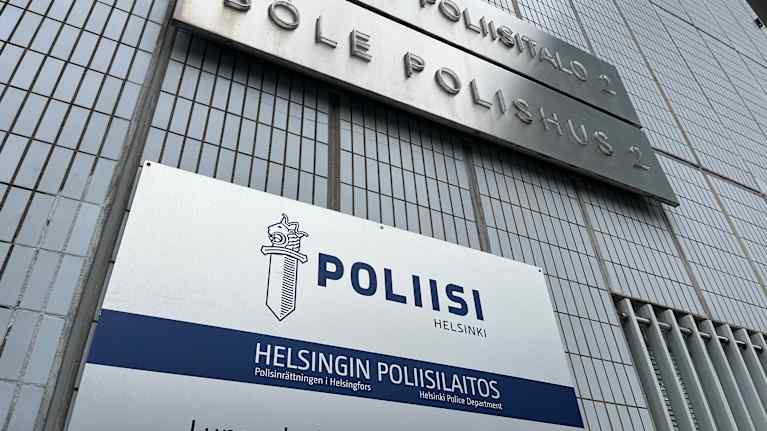 Vaaleansinisessä seinässä on kyltti, joissa lukee Helsingin poliisilaitos eri kielillä sekä osittain kyltti, lukee poliisitalo 2. 