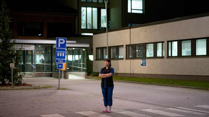 Sinupukuinen hoitaja seisoo autiolla sairaalan pihalla.