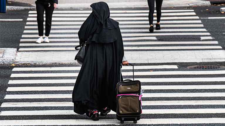 Nainen pukeutuneena burkaan ylittää suojatietä.
