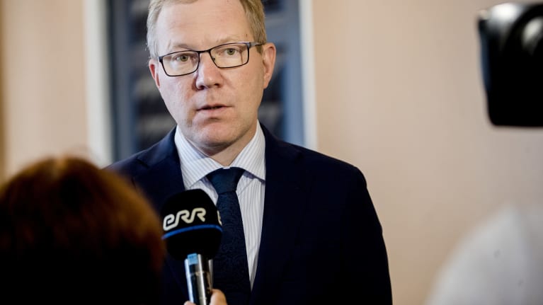 Silmälasipäinen mies sinisessa pikkutakissa antaa haastattelua