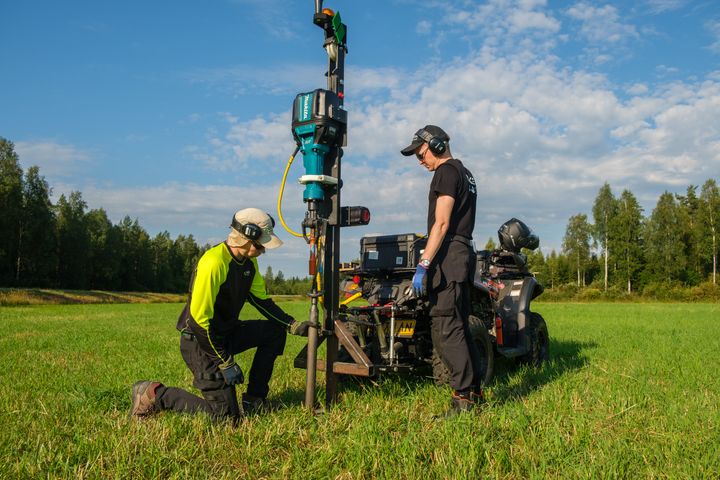 Kaksi%20henkil%F6%E4%20ty%F6skentelee%20ulkona%20pellolla%20maaper%E4n%20mittaamiseen%20liittyv%E4n%20laitteen%20kanssa.%20Toinen%20henkil%F6%20on%20polvistuneena%2C%20ja%20taustalla%20n%E4kyy%20mets%E4%E4.