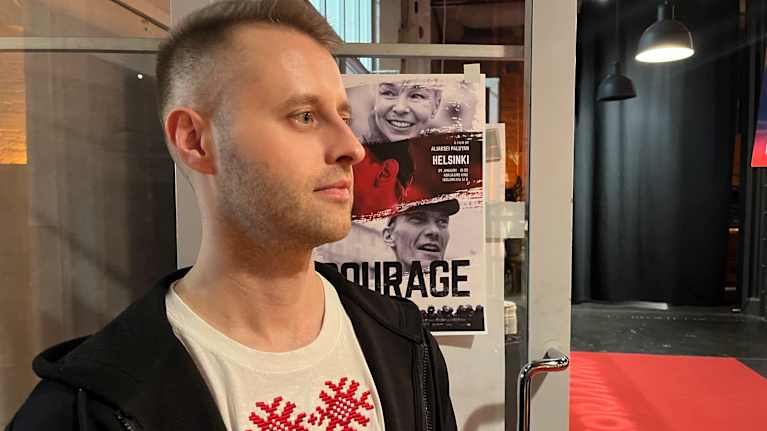 Suomen Valkovenäläisten Järjestön puheenjohtaja Kyril Kirylau seisoo Courage-elokuvan julisteen edessä.