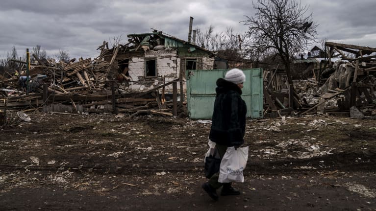 Mustiin pukeutunut nainen kävelee kuolleessa maisemassa. Käsissä muovikassit.