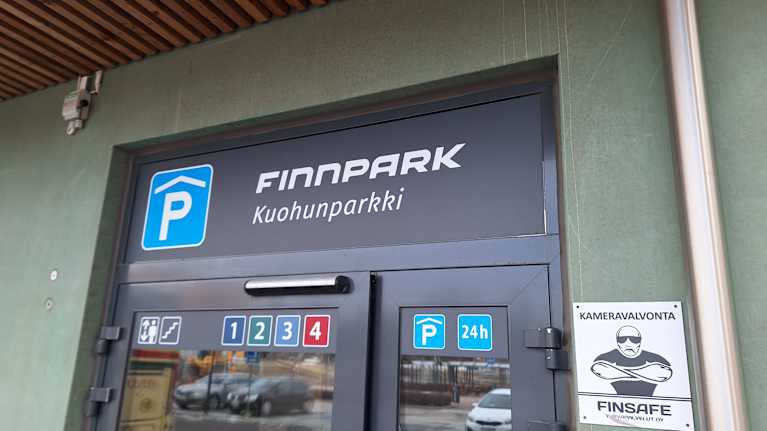 Pysäköintitalon ovi kuvattuna ulkoa. Oven yläpuolella lukee "Finnpark, Kuohunparkki"