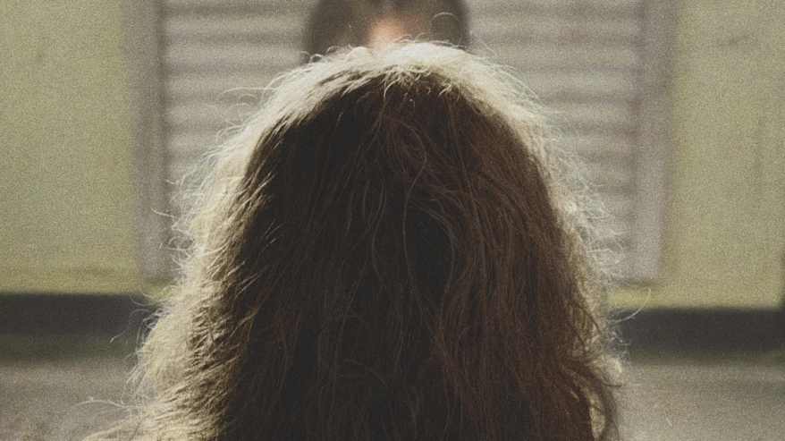 Pitkähiuksisen ihmisen takaraivo, takana toisen ihmisen pään yläosa.