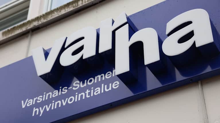 Varhan, eli Varsinais-Suomen hyvinvointialueen kyltti Uudenkaupungin terveyskeskuksen ja sairaalan seinässä pääoven päällä.