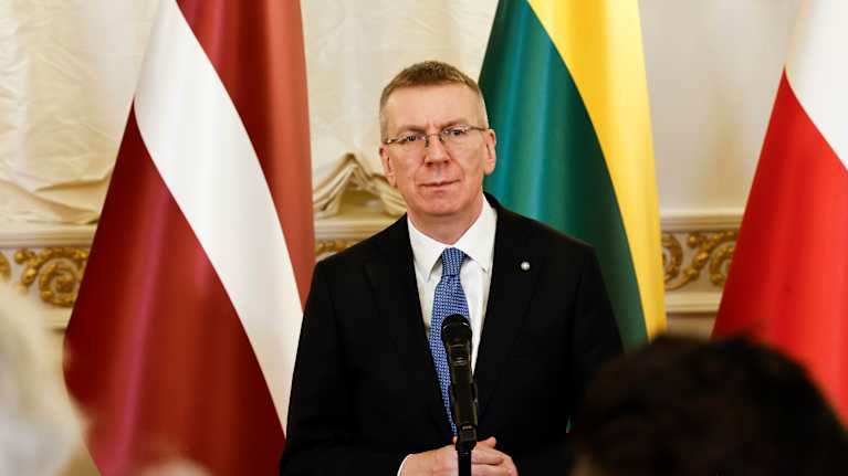 Edgars Rinkēvičs puhuu mikrofoniin median edessä. Taustalla Latvian, Liettuan ja Puolan liput.