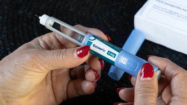 Naisen käsissä vaaleansininen injektiokynä piikki avattuna ja kyljessä lukee Ozempic 1mg.