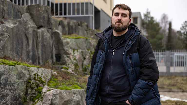 Mies seisoo kivien edessä ulkona pukeutuneena siniseen toppatakkiin.