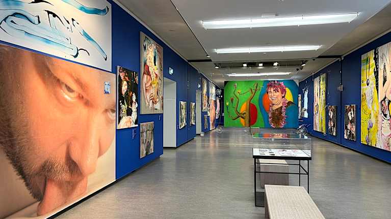 Taidemuseon siniseinäisessä näyttelytilassa esillä värikkäitä teoksia.
