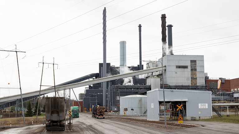 Harmaista nelsikanttisista rakennuksista ja savupiipuista koostuva paperitehdas pilvisenä päivänä.
