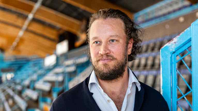 Henkilö seisoo tyhjillä katsomoalueilla, taustalla näyttäytyy urheilustadionin istumapaikkoja ja metallisia rakenteita.