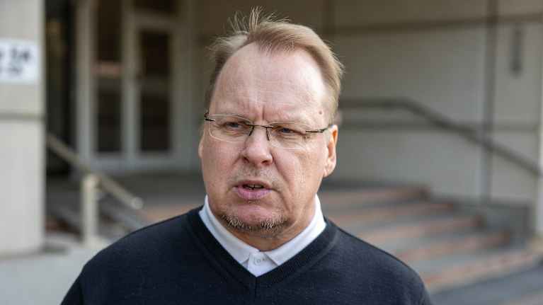 Silmälasipäinen mies puolilähikuvassa toimistorakennuksen edustalla.