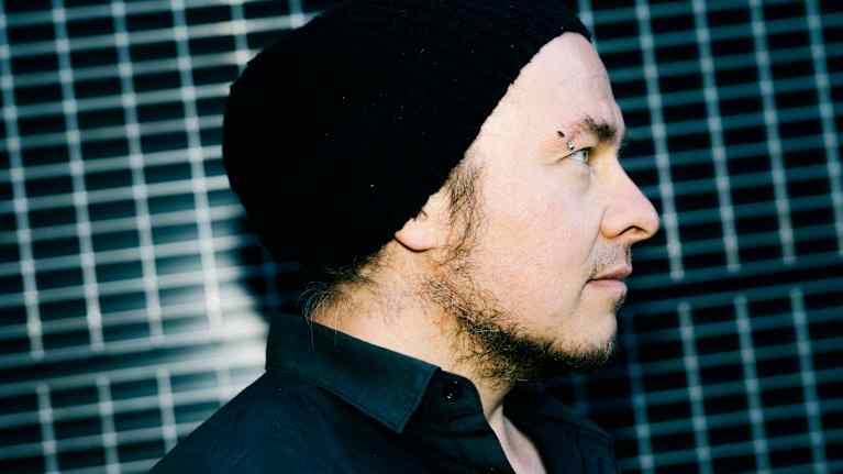 Mies seisoo ritiläseinän edessä ja hänellä on yllään musta kauluspaita.