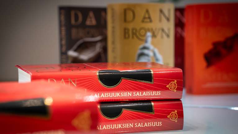 Kaksi Dan Brownin salaisuuksien salaisuus -romaania päällekkäin. Taustalla sumeana muita hänen kirjojaan.