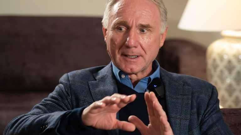 Kirjailija Dan Brown katsoo alaviistoon kädet rinnan korkeudella.