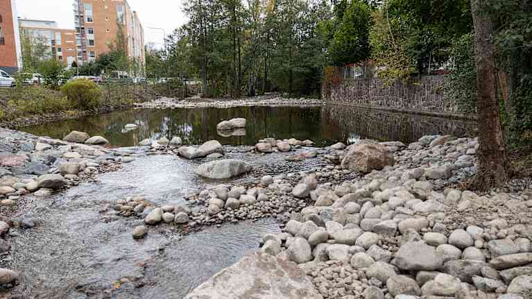 Etualalla pyörillä kivillä reunustettu ja pohjustettu uoma, jonka yläpuolella parikymmentä metriä leveä allas.