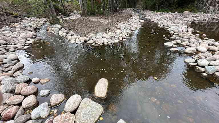 Kaksi kapeata pyöreiden kivien reunustamaa purouomaa, jotka yhdistyvät yhdeksi isommaksi.