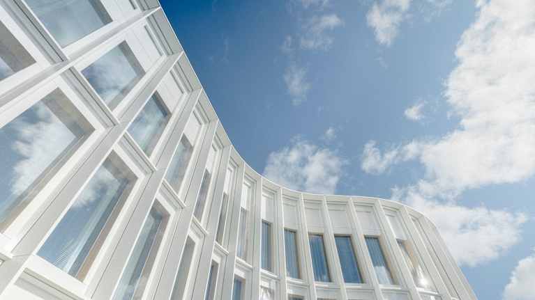 Moderni rakennus heijastaa sinistä taivasta suurista ikkunoistaan. Arkkitehtuurille ominaista on valkoiset, pystysuuntaiset elementit.