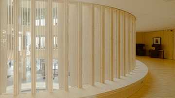 Modernin rakennuksen sisätila, jossa on kaareva seinä, joka on tehty pystysuorista puisista elementeistä ja lasista. 