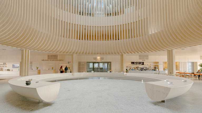 Valoisa ja avara sisäänkäyntiaula  jossa erottuu suuren kaaren muotoinen istuma-alue ja moderni arkkitehtuuri.