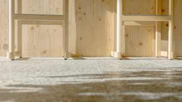 Puinen seinä ja huonekalu, jonka varjot heijastuvat harmaalle laattalattialle.