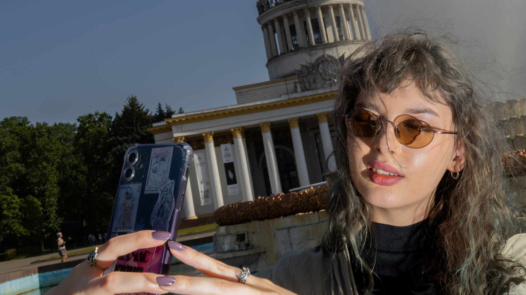 Marta ottaa selfietä. Takana neuvostoaikainen monumentaalinen rakennus.