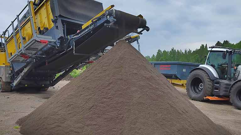 Hiekkaa lajitteleva kone kuljettaa hihnalla hiekkaa, joka on tuottanut tasaisesti kartiomuotoon kasatun hiekkakasan. 