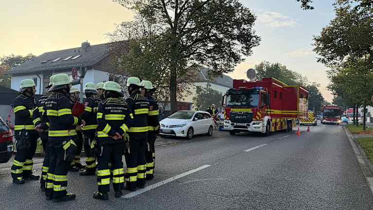 Palopelastajia keskustelee ringissä autotiellä. Taustalla omakotitaloja ja paloautoja.
