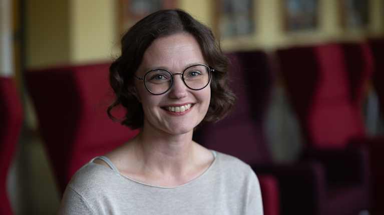 Mona Mannevuo istuu punaisten tuolien edessä.