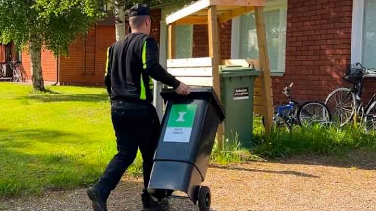Mies vie biojäteastiaa punatiilisen talon pihalle. 