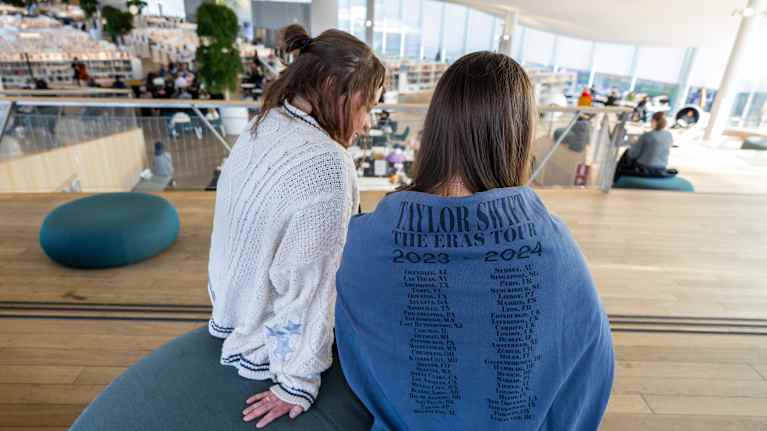 Kaksi naistaistuu Helsingin keskustakirjasto Oodin yläkerrassa, toinen heistä pukeutuneena Taylor Swiftin kiertuetta mainostavaan huppariin, jossa kiertueen päivämäärät ovat esillä.