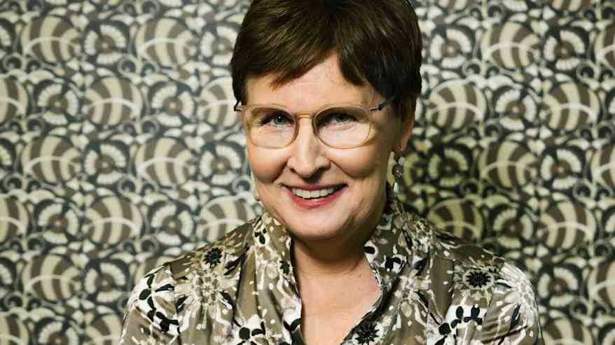 Nainen istuu penkillä kuviollista taustaseinää vasten.