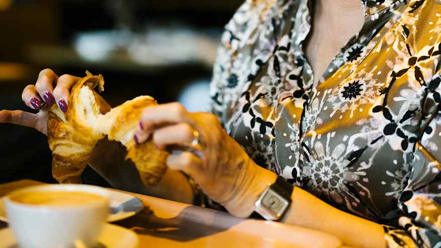 Nainen nauttii kahvia ja croissantia kahvilassa.