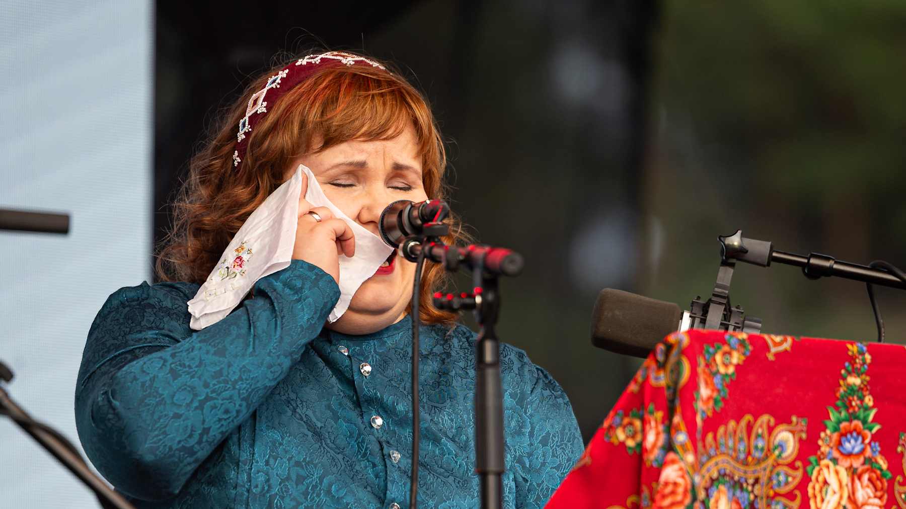 Nainen itkee itkuvirttä lavalla, hieroen silmäkulmaansa nenäliinaan. Anna Lumikivi. 