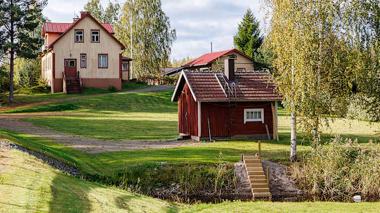 Keltainen puusta rakennettu asuintalo piharakennuksineen syksyisessä maisemassa Luhangan kirkonkylällä.