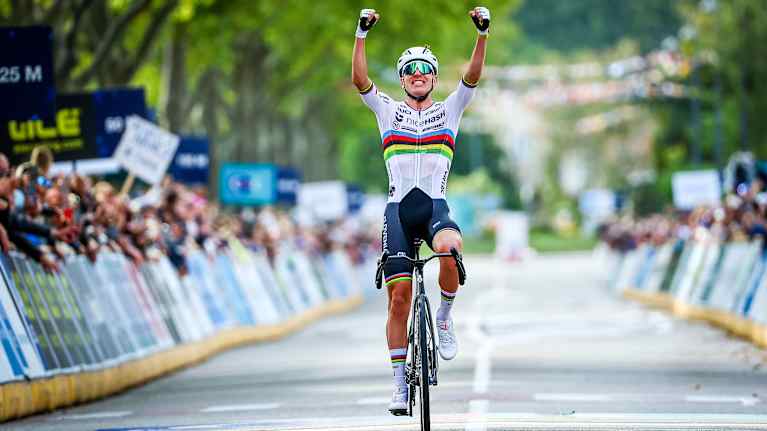 Maantiepyöräilijä ylittää maaliviivan kädet ylhäällä.