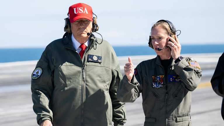 Trump kävelee lentotukialuksen kannella naisen vierellä.