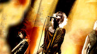 Mies laulaa ja soittaa kitaraa lavalla, taustalla sekä oikealla puolella näkyy yhtyeen muita jäseniä kitaroineen.