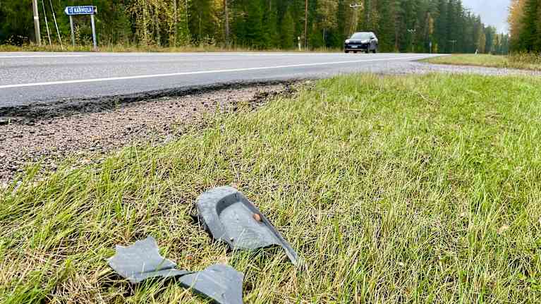 Tienpientareella on rikkoutuneita muoviosia ja taustalla ajaa auto.
