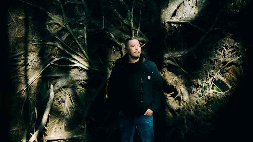 Henkilö seisoo metsän keskellä, valonsäteiden loisteessa, joka korostaa puun oksien kuvioita.