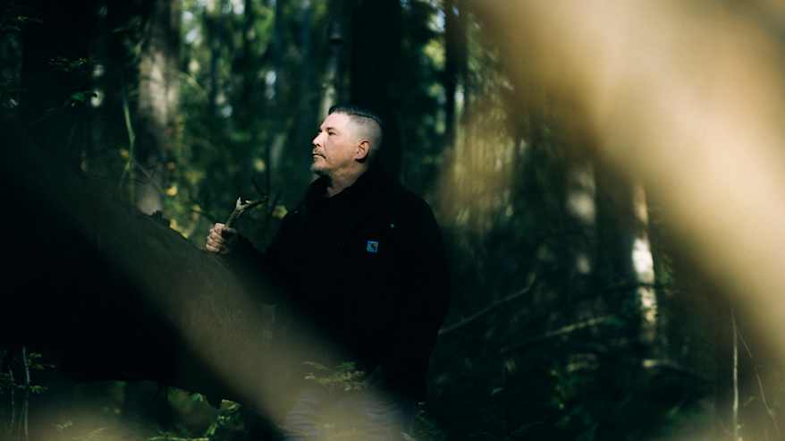 Henkilö seisoo metsän keskellä, valonsäteiden loisteessa, joka korostaa puun oksien kuvioita.