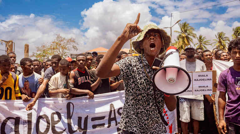 Mielenosoittajia megafonin ja banderollien kanssa kadulla.