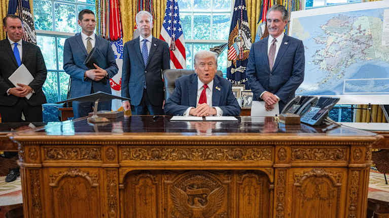 Vanha mies valkoisessa talossa, taustalla neljä pukumiestä.