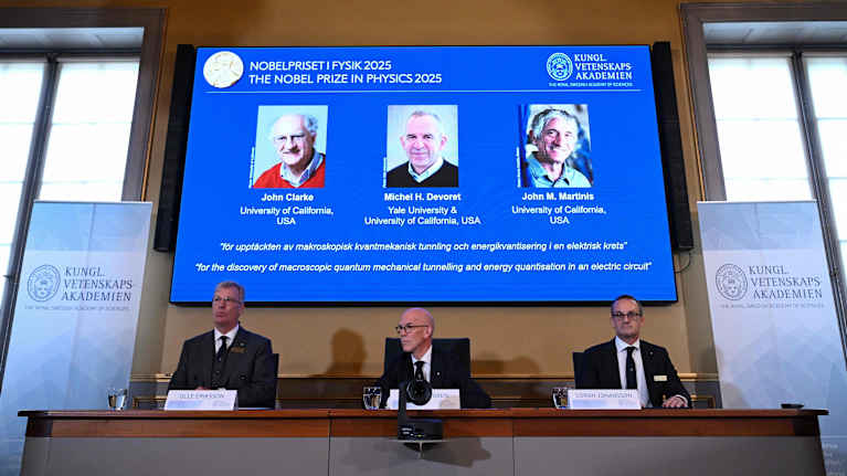 Fysiikan Nobel-palkittujen kuvat valkokankaalla valintaraadin jäsenten takana.