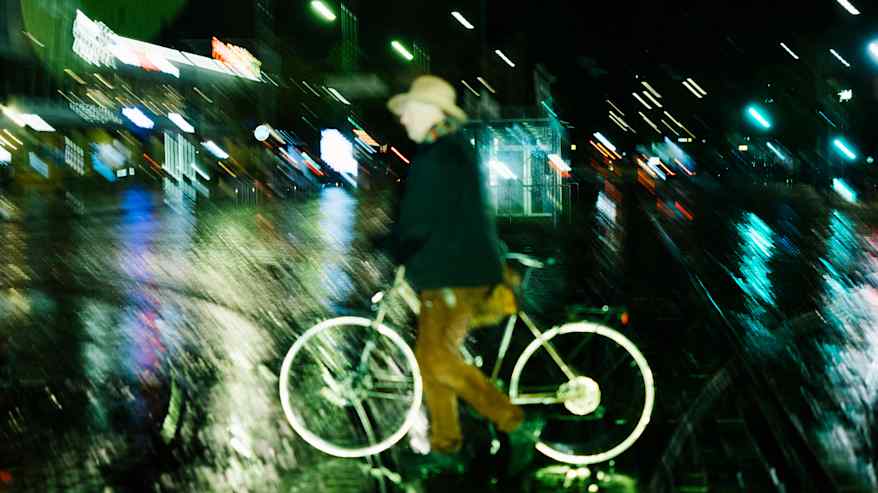 Pyöräilijä ylittää katua sateisena iltana.
